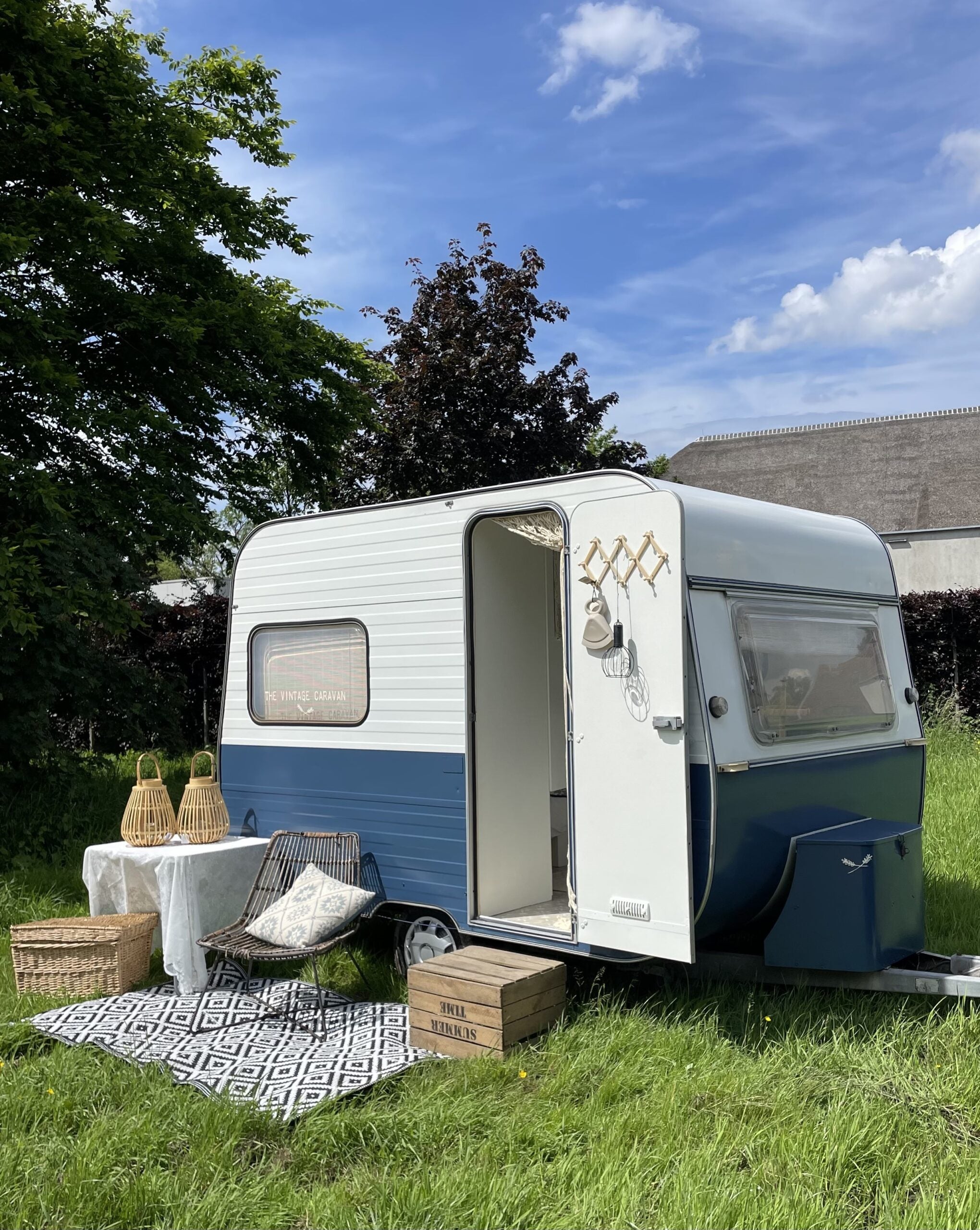 Charming Adria 305 caravan in a grassy setting, featuring a blue and white exterior, outdoor seating, and decorative accessories.