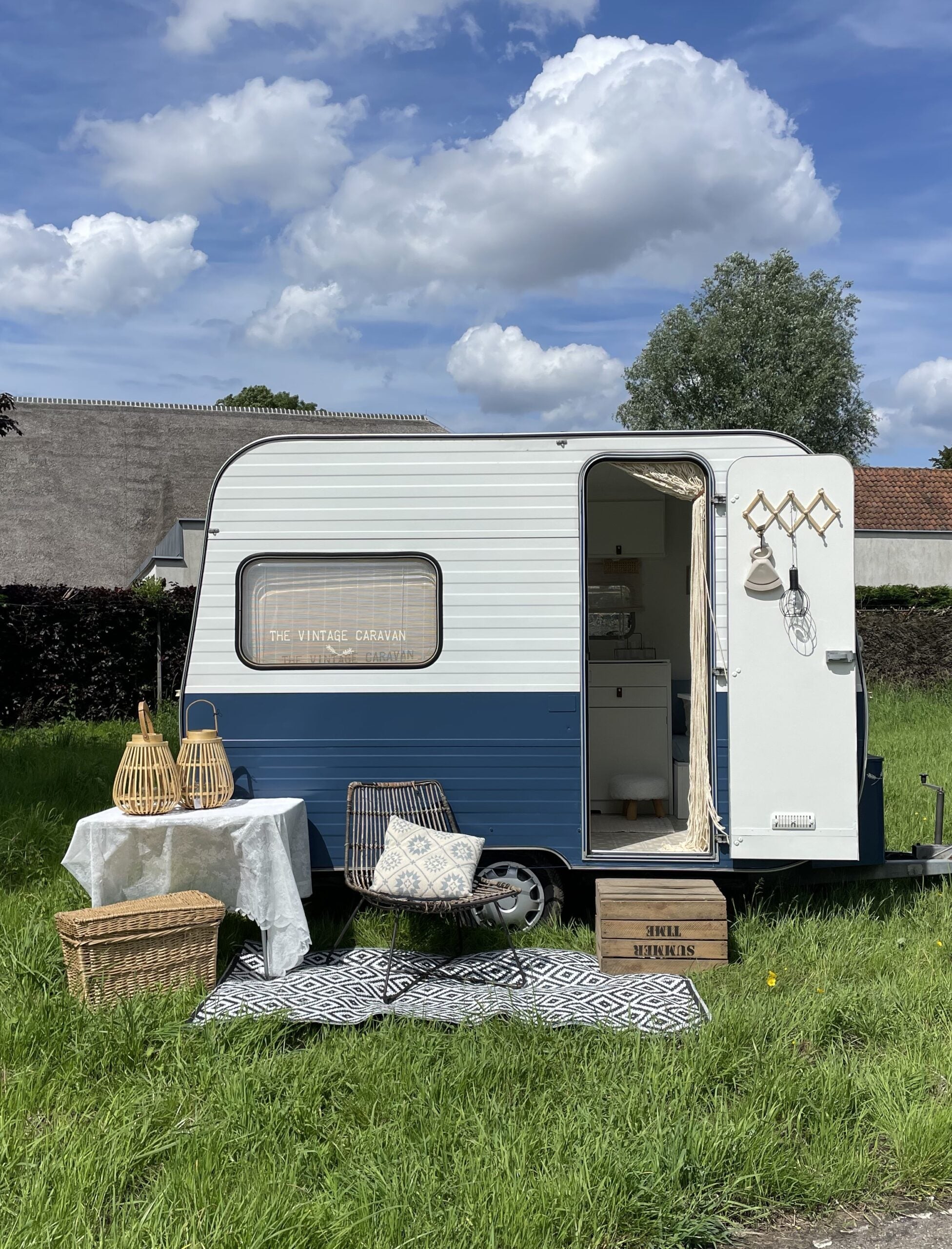 Charming Adria 305 caravan in blue and white, set in a grassy area with decorative elements and outdoor furniture.
