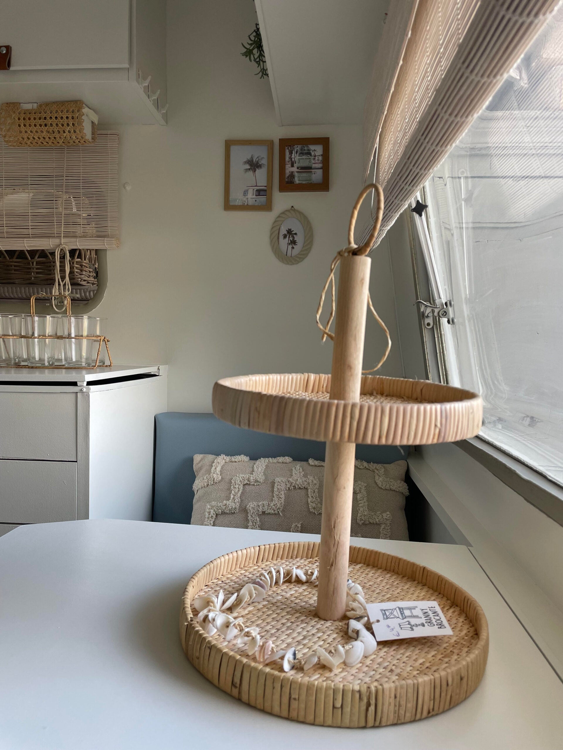 Two-tiered bamboo serving stand with seashells, set on a white table in a cozy caravan interior.