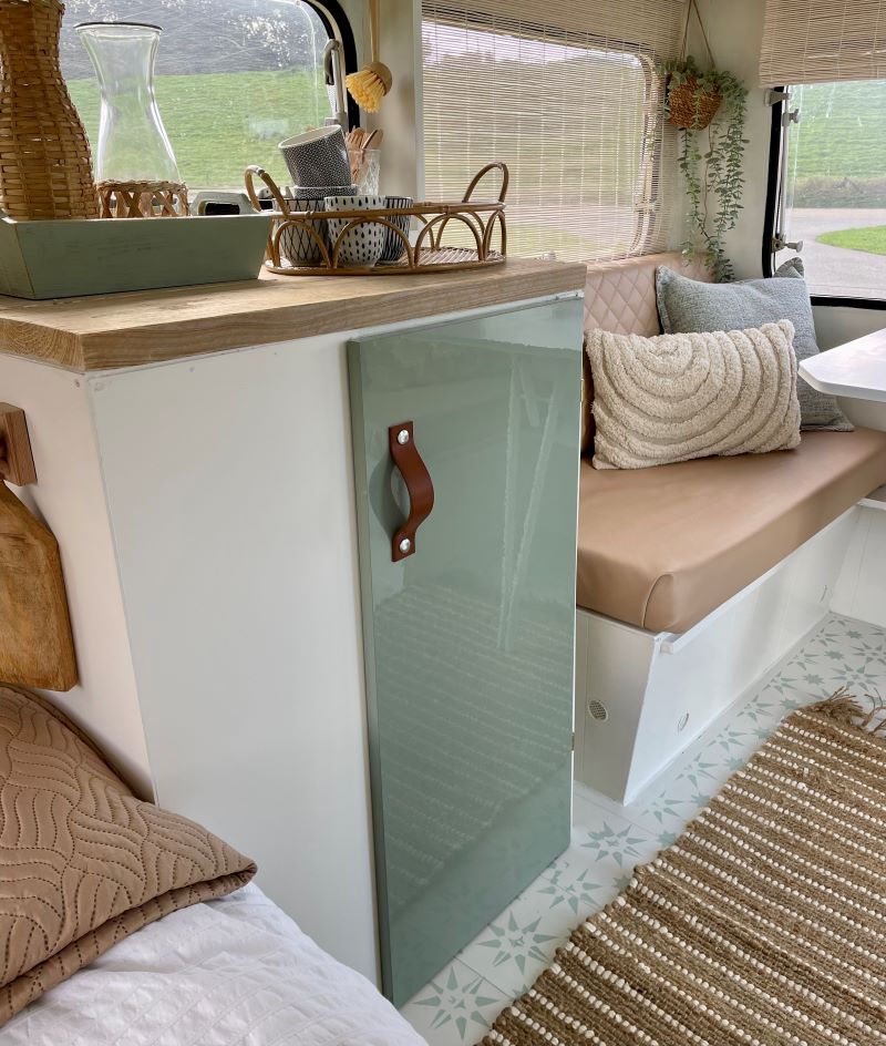 Sleek green cabinet with a brown handle in a cozy caravan interior featuring beige cushions and decorative items.