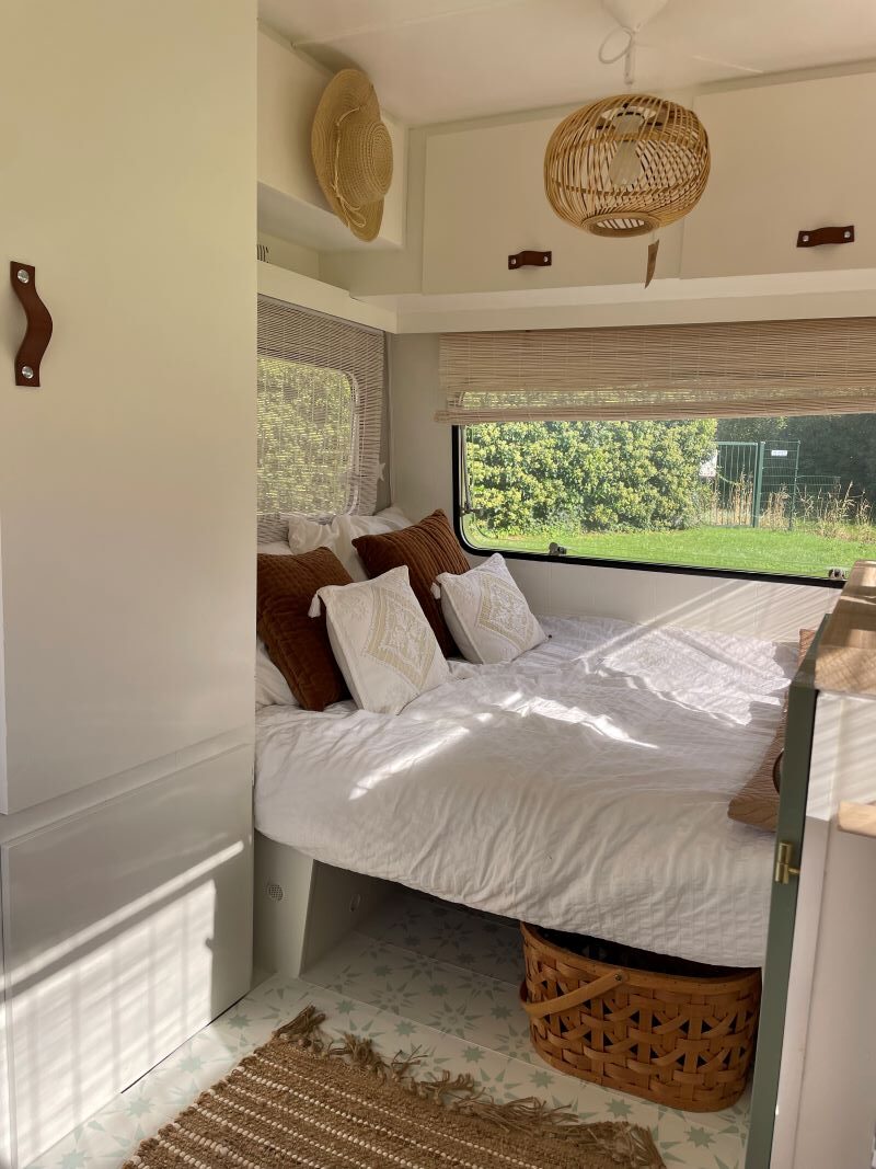 Cozy interior of the Chateau 320 caravan featuring a queen bed with textured pillows, natural light, and woven decor.