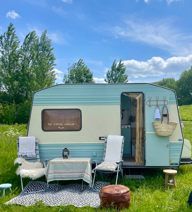 Vintage Bűrstner City caravan in a grassy field, featuring cozy outdoor seating and a bright blue sky.